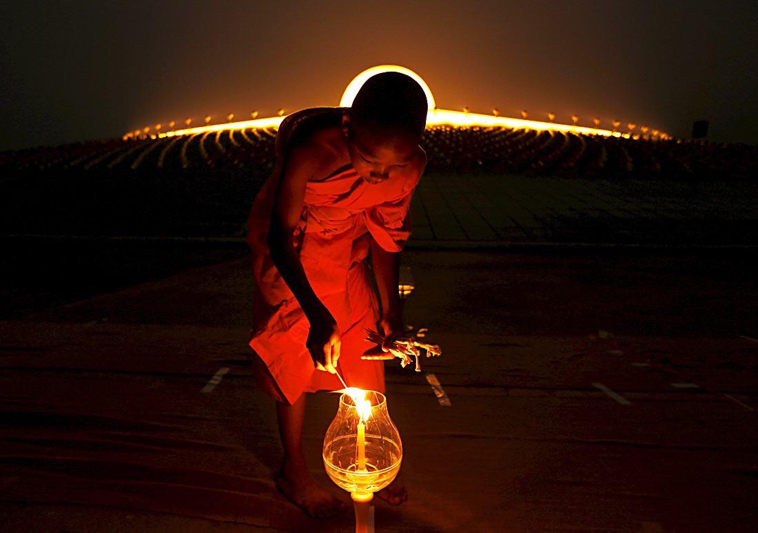 Патхумтхани, Таиланд. На куполе храма Ват Пхра Дхаммакая стоит 300 тысяч золотых  статуэток Будды. Еще 700 тысяч —  внутри храма. На фото: монах зажигает свечу в день почитания Будды,  праздник Макха Буча.