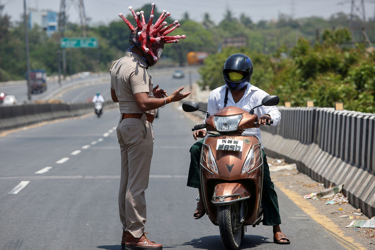 Полицейский Раджеш Бабу в шлеме с изображением коронавируса просит человека оставаться дома во время 21-дневного общенационального карантина, чтобы ограничить распространение коронавируса. Ченнаи, Индия, 28 марта 2020 года