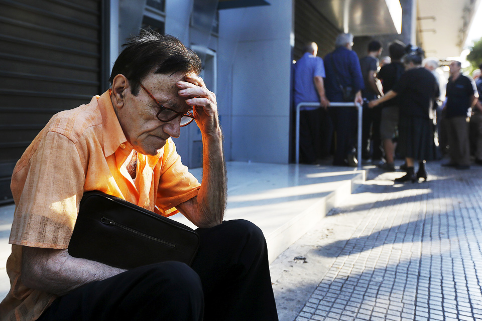 77-летний пенсионер сидит у закрытого банка. Ранее Евросоюз обещал помочь Греции в обмен на сокращение зарплат и снижение пенсий