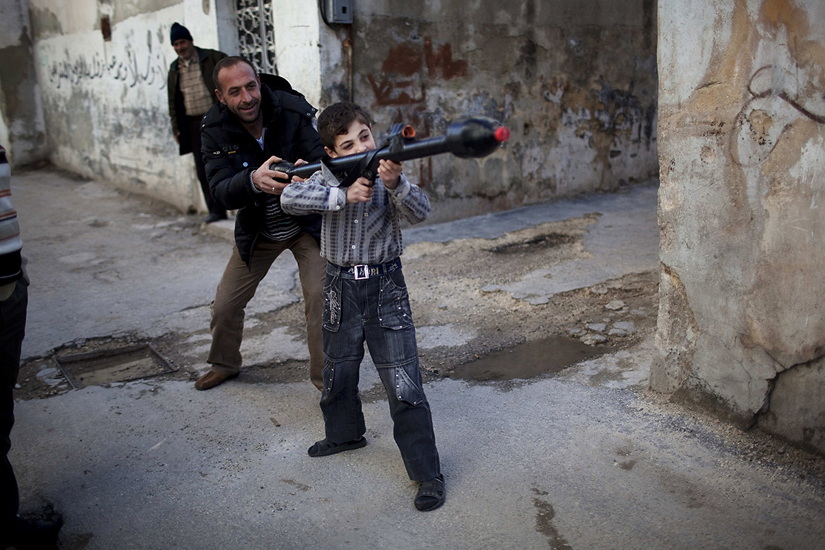 Мужчина учит 11-летнего Билала обращаться с игрушечным ручным противотанковым минометом в сирийской провинции Идлиб в марте 2012 года. Эта фотография — часть серии аргентинского фотографа Родриго Абда, снимавшего сирийскую войну.