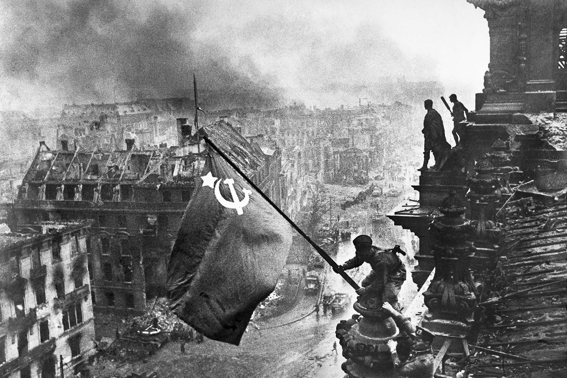 Бойцы 8-й гвардейской армии РККА Алексей Ковалев и Абдулхаким Исмаилов (слева направо) с красным знаменем на крыше здания Рейхстага после взятия города советскими войсками, 2 мая 1945 года